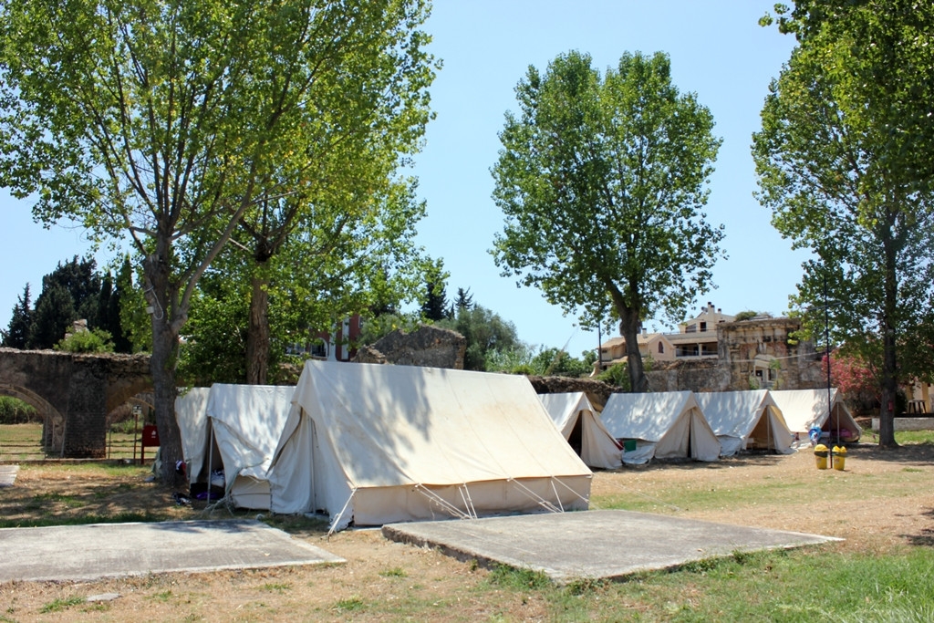 Εικόνα από τις κατασκηνώσεις στα Γουβιά στην Κέρκυρα που απεικονίζει σκηνές ανάμεσα σε δέντρα στην εξοχή.